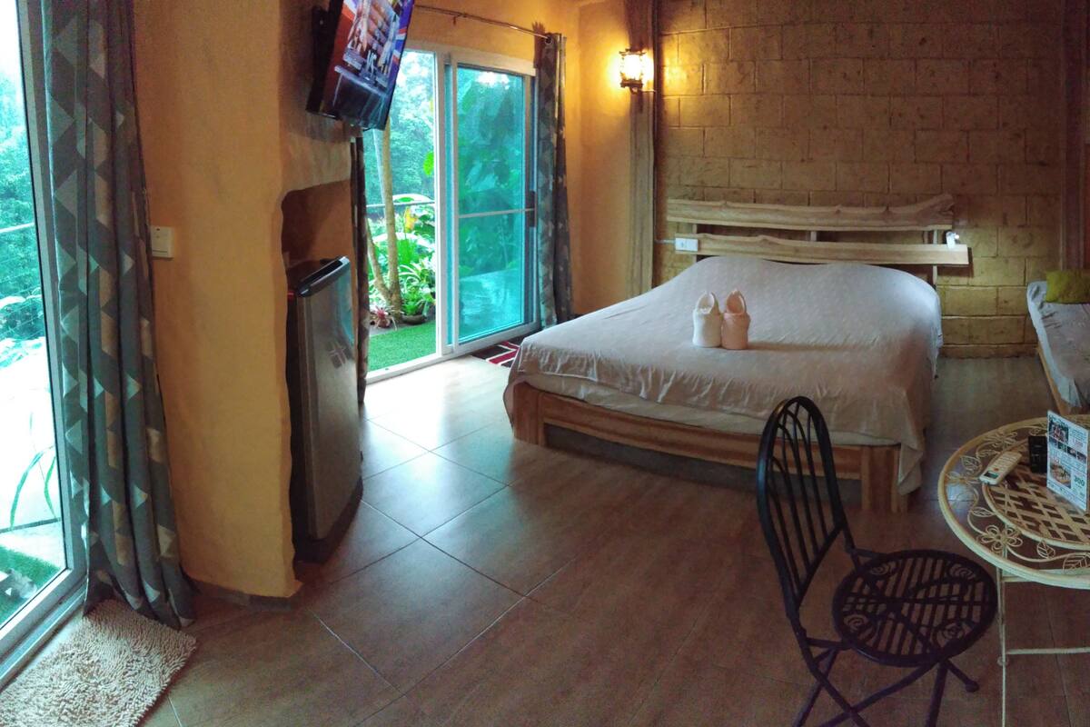 Une chambre à coucher avec un lit, une petite table et une chaise, un téléviseur et une fenêtre avec des rideaux.