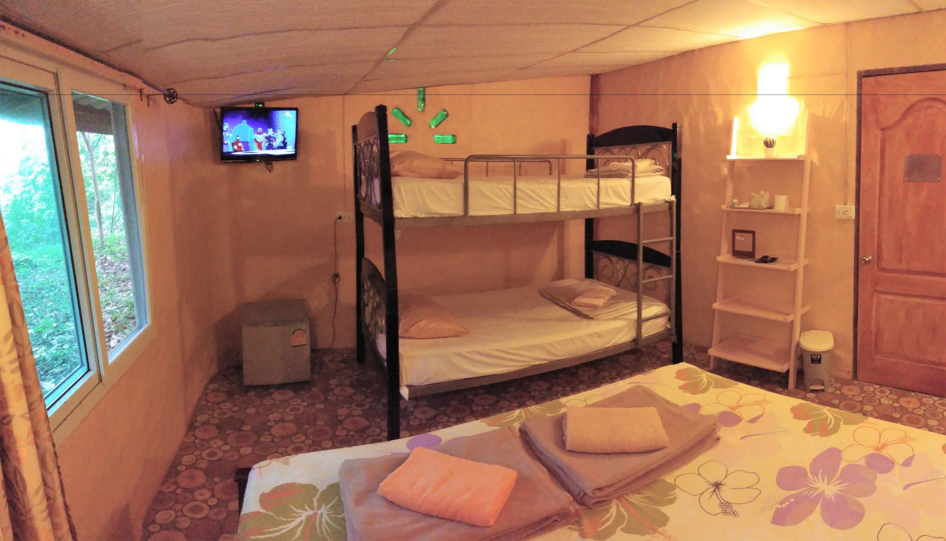 A bunk bed room with a television, a small cabinet, and a bedside table with a lamp.