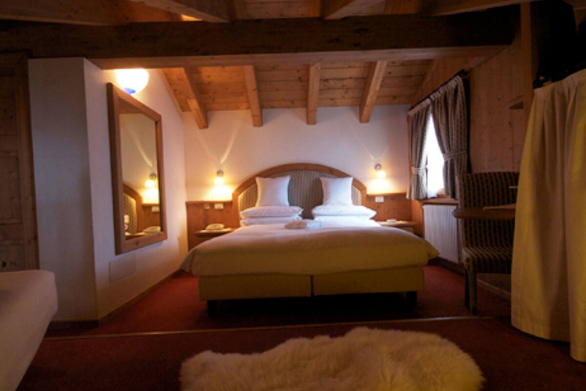 Ein gemütliches Schlafzimmer mit einem großen Bett, Holzbalken, einem Spiegel, Nachttischlampen und einem Fellteppich.