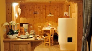A cozy wooden interior with a dining area, a kitchen counter with a tray of food, and a potted plant. - Hotel Baita Fiorita (Valfurva)