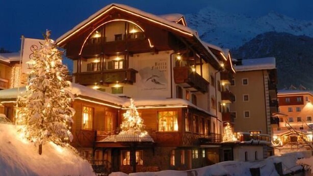 A multi-story hotel with balconies, a snow-covered landscape, and a river in the foreground. - Hotel Baita Fiorita (Valfurva)