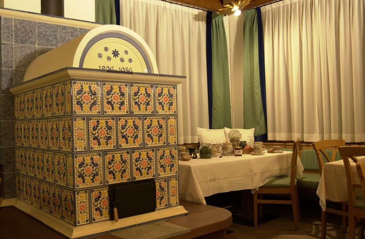 A traditional kitchen with a tiled stove, a table set with tea service, and a dining area with chairs.