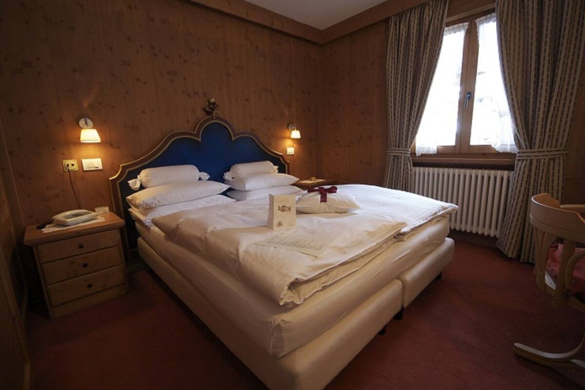Ein Hotelzimmer mit einer holzverkleideten Wand, einem blauen Kopfteil, einem Bett mit weißer Bettwäsche, einem Nachttisch mit Telefon und einem Vorhangfenster.
