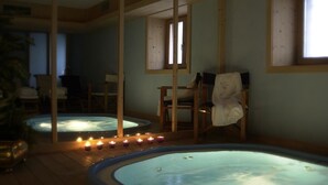A spa area with two hot tubs, wooden beams, and candles. - Hotel Baita Fiorita (Valfurva)