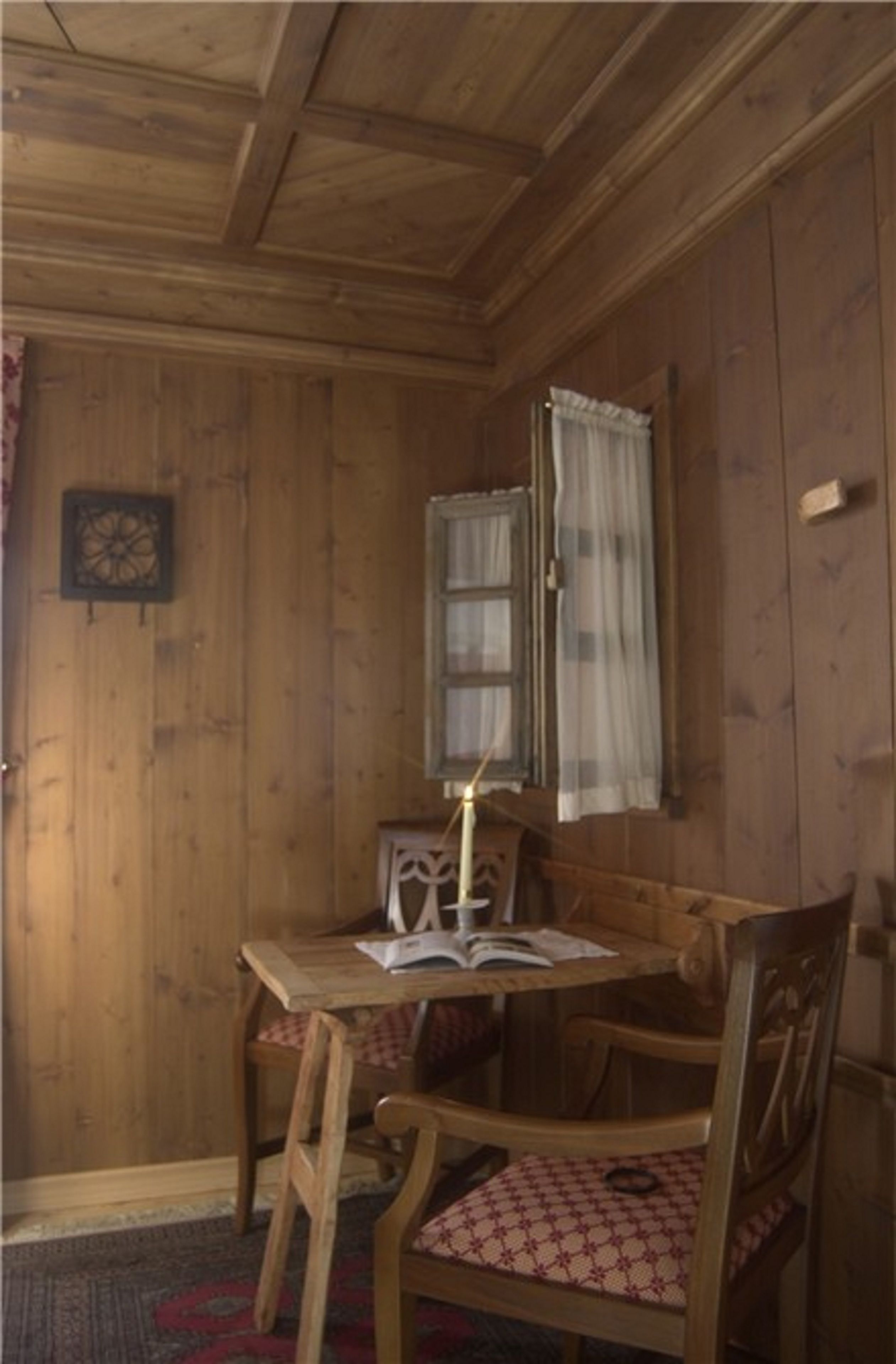 Une pièce en bois, avec une table, deux chaises, un livre et une bougie.