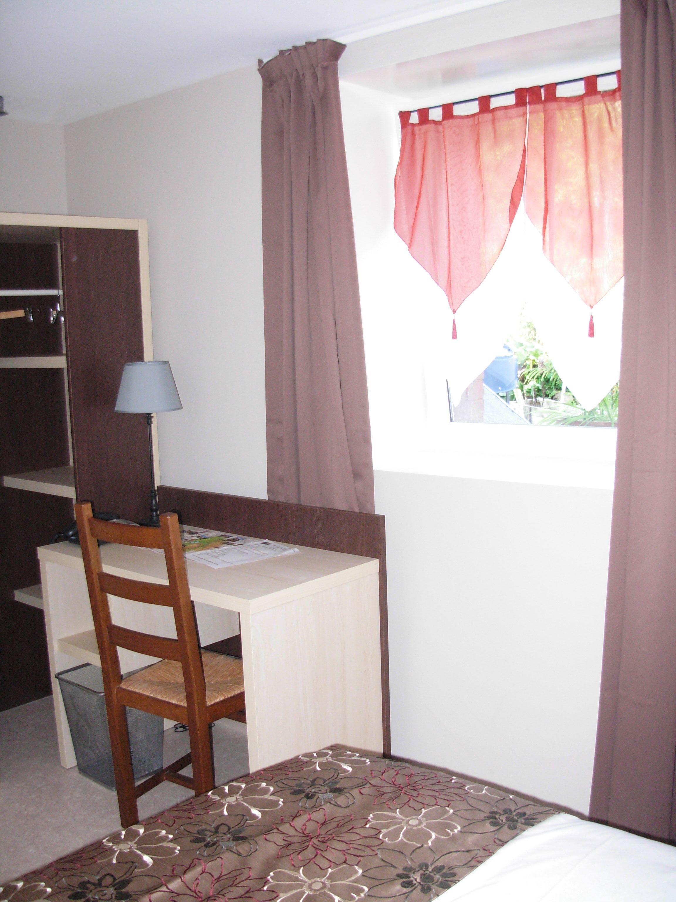 A bedroom with a single bed, a desk with a chair, a wardrobe, and a window with curtains.