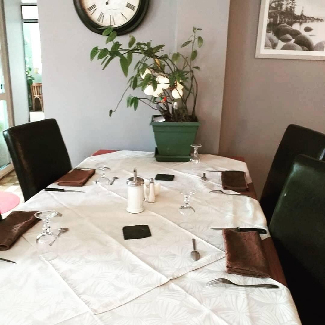 Mesa de comedor con mantel blanco, platos, cubiertos y una planta en maceta.