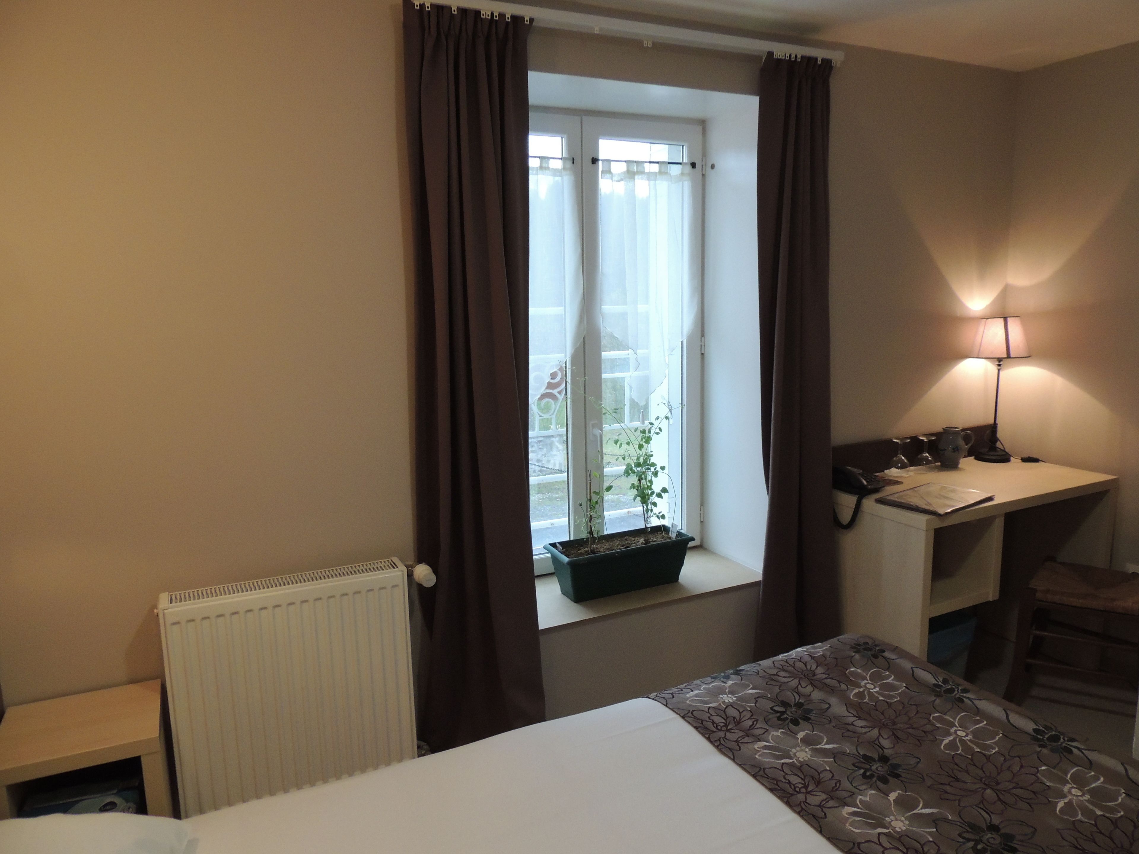 Ein Hotelzimmer mit einem Bett, einem Schreibtisch mit Lampe, einem Fenster mit Vorhängen und einem Heizkörper.
