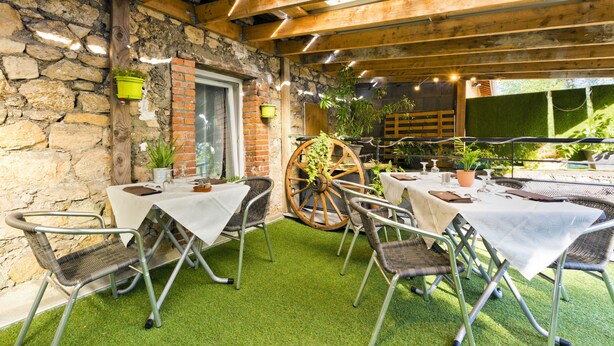 An outdoor patio with tables and chairs, a wooden ceiling, stone walls, and potted plants. - Hotel Restaurant De La Dore (Vertolaye)