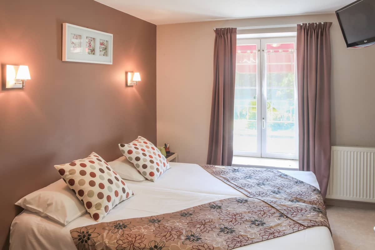 Een hotelkamer met een bed, twee wandlampen, een lijst, een raam met gordijnen en een televisie aan de muur.
