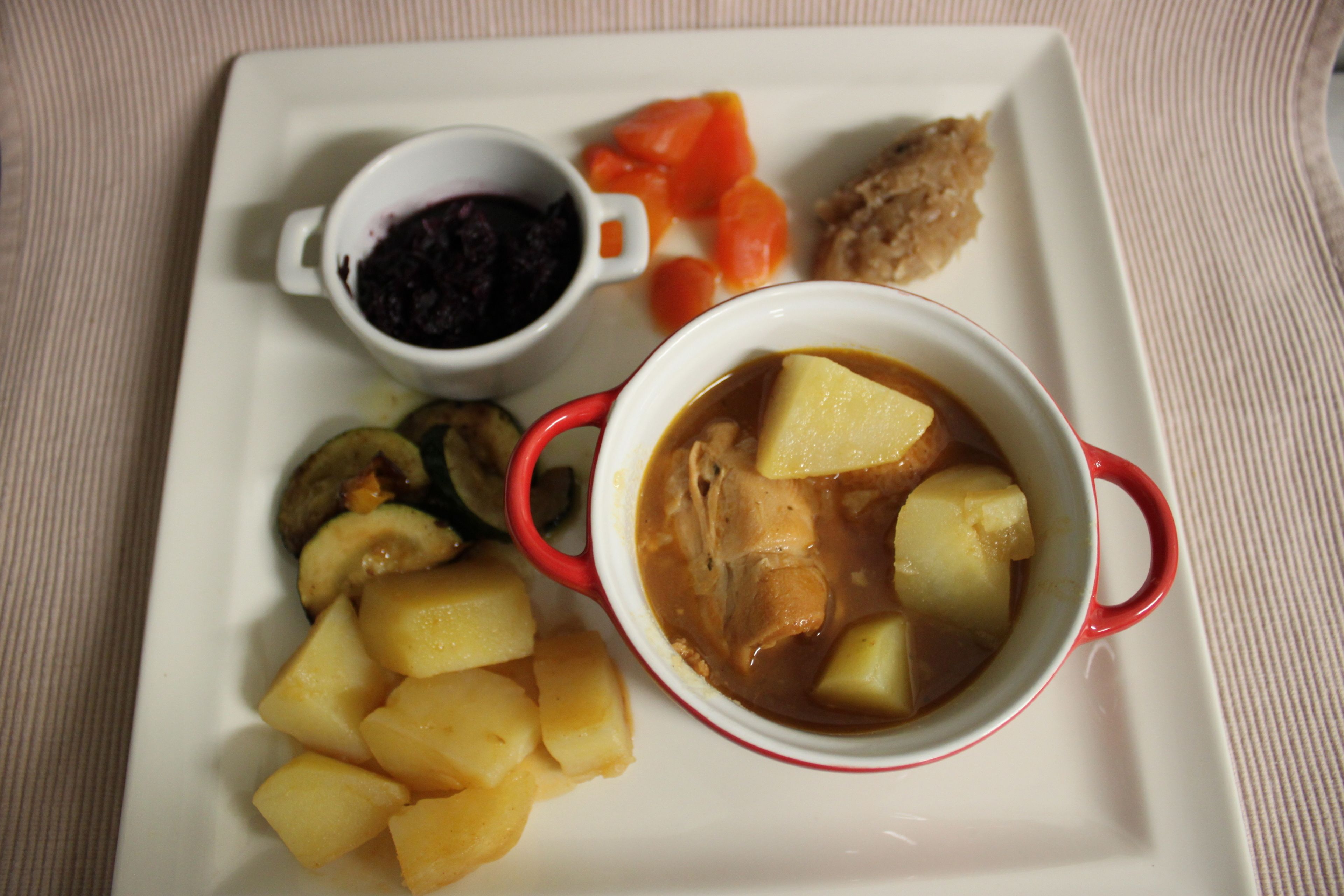 Une assiette contenant un ragoût, des pommes de terre, des carottes et un petit bol de sauce.