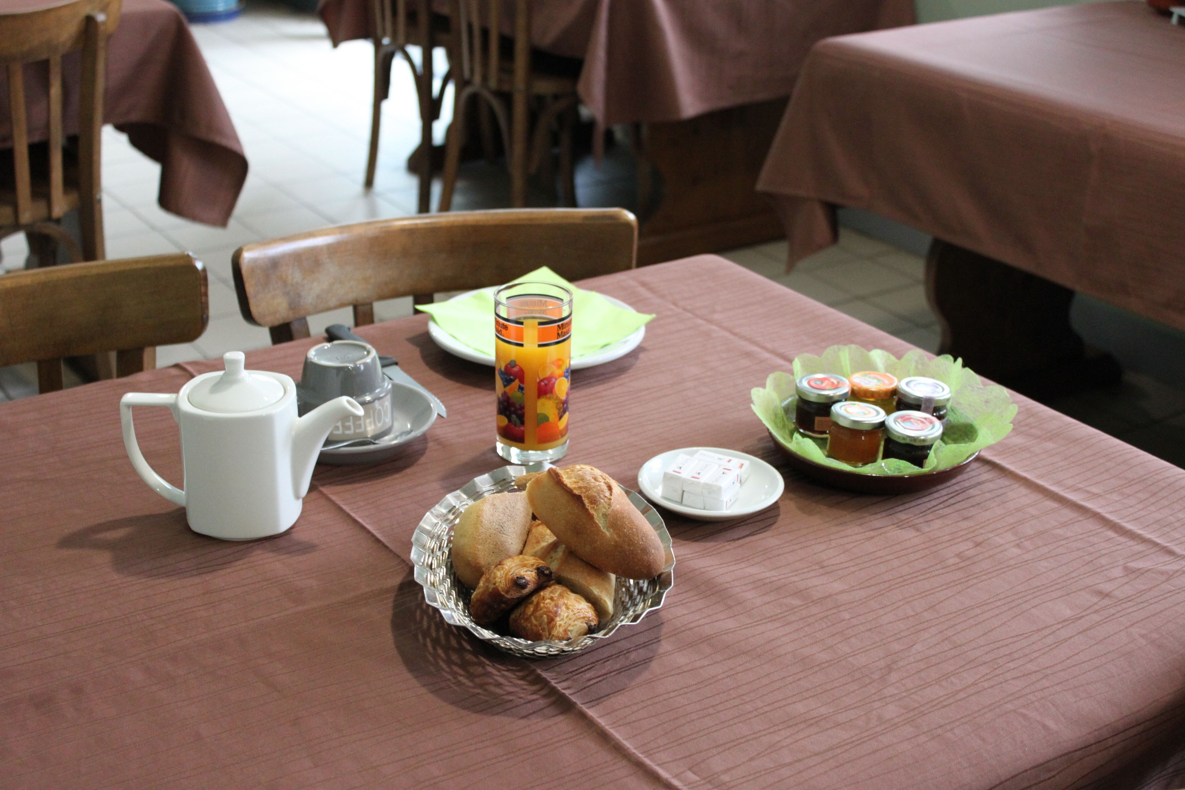 A breakfast table with a teapot, a glass of orange juice, a plate of pastries, and a plate of jam.