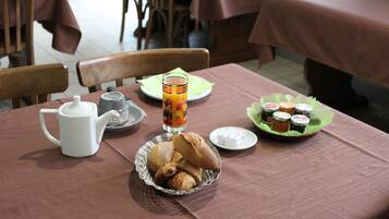 A breakfast table with a teapot, a glass of orange juice, a plate of pastries, and a plate of jam.