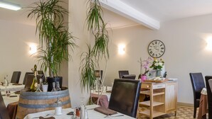 A dining area with tables set for two, featuring a wooden barrel centerpiece, potted plants, and a wall clock. - Hotel Restaurant De La Dore (Vertolaye)