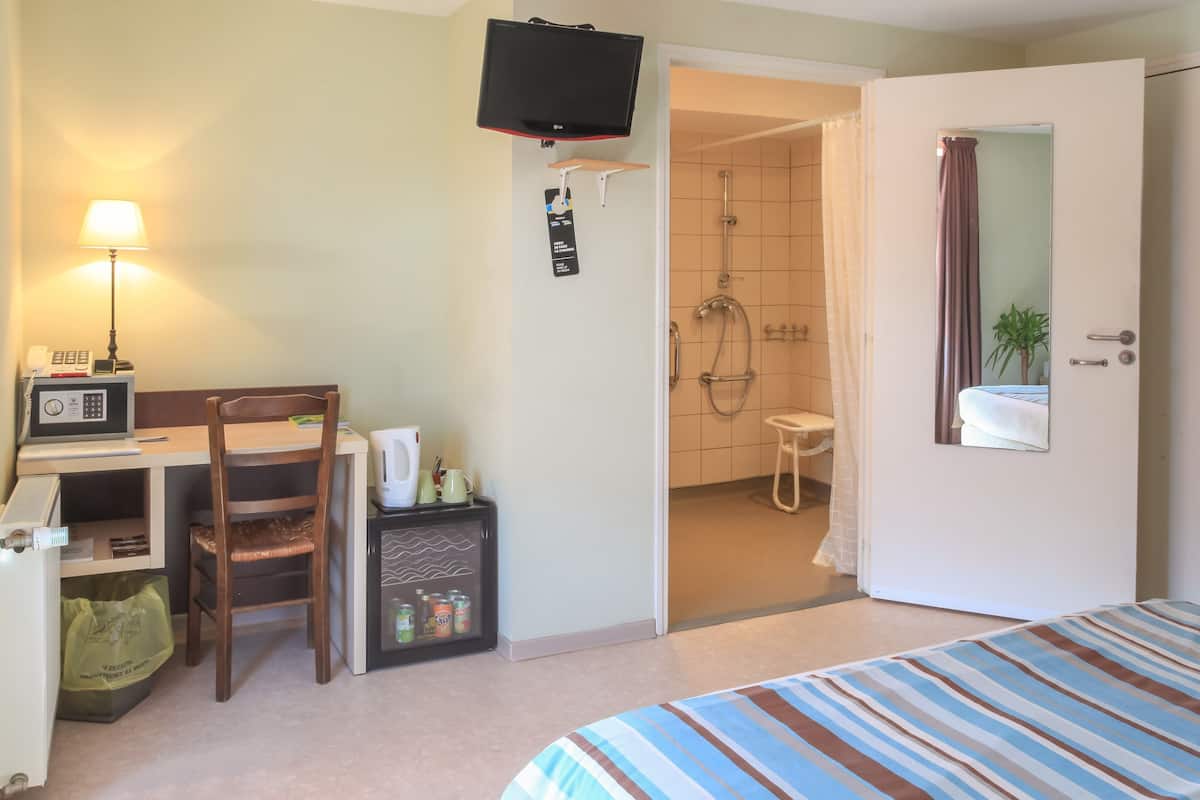 Een hotelkamer met een bed, bureau, stoel, televisie en een douche.