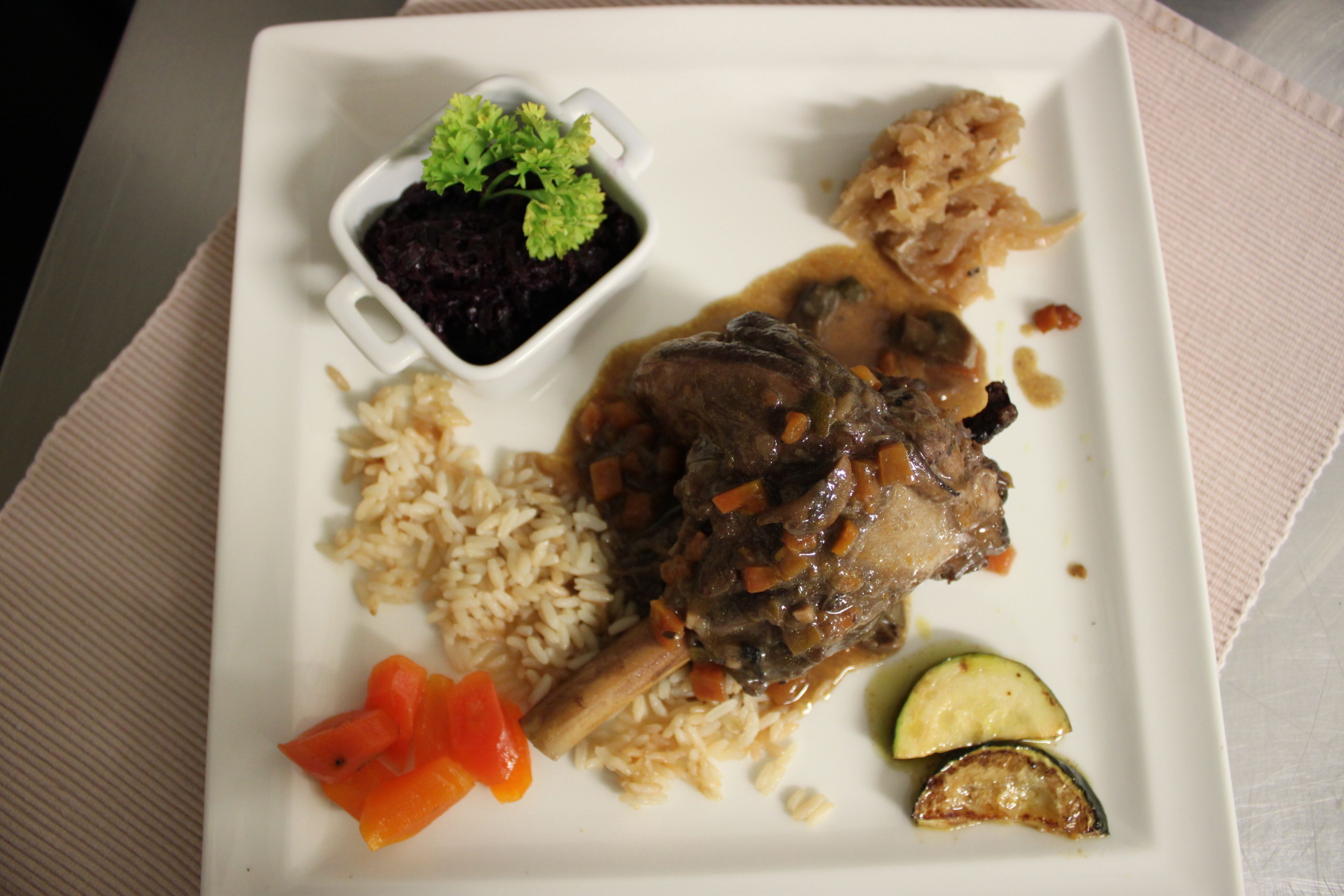 Une assiette contenant un plat de viande, du riz, des légumes et un petit bol de sauce.