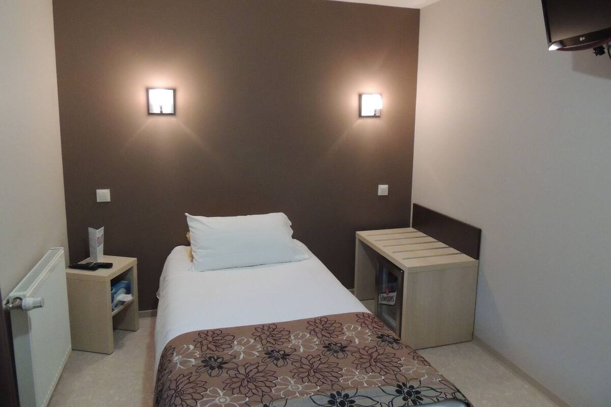 Een hotelkamer met een bed, nachtkastjes, een radiator en een aan de muur bevestigde televisie.