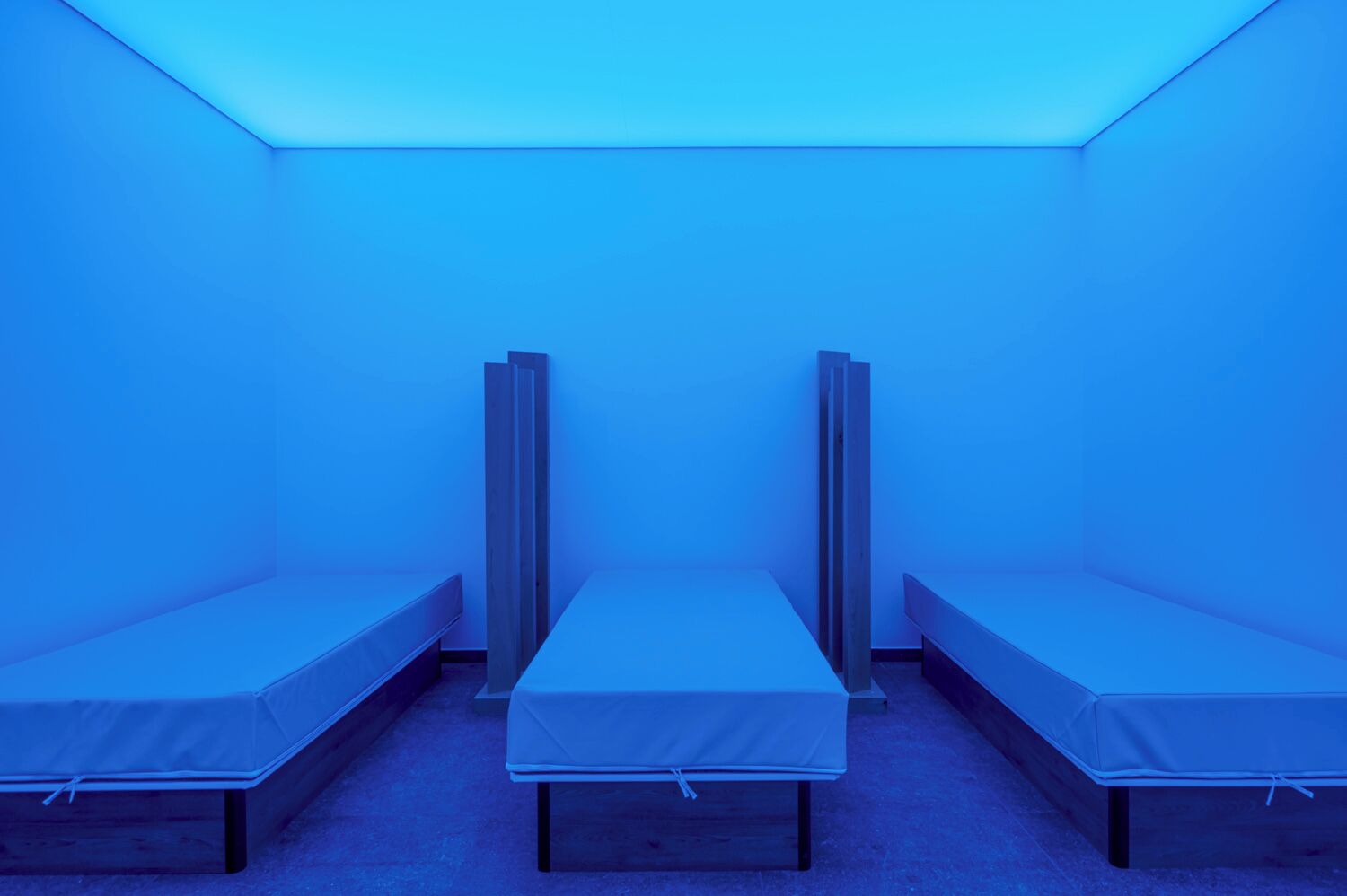 Une chambre avec trois lits simples alignés contre un mur, chacun étant équipé d’un matelas et d’un cadre en bois.