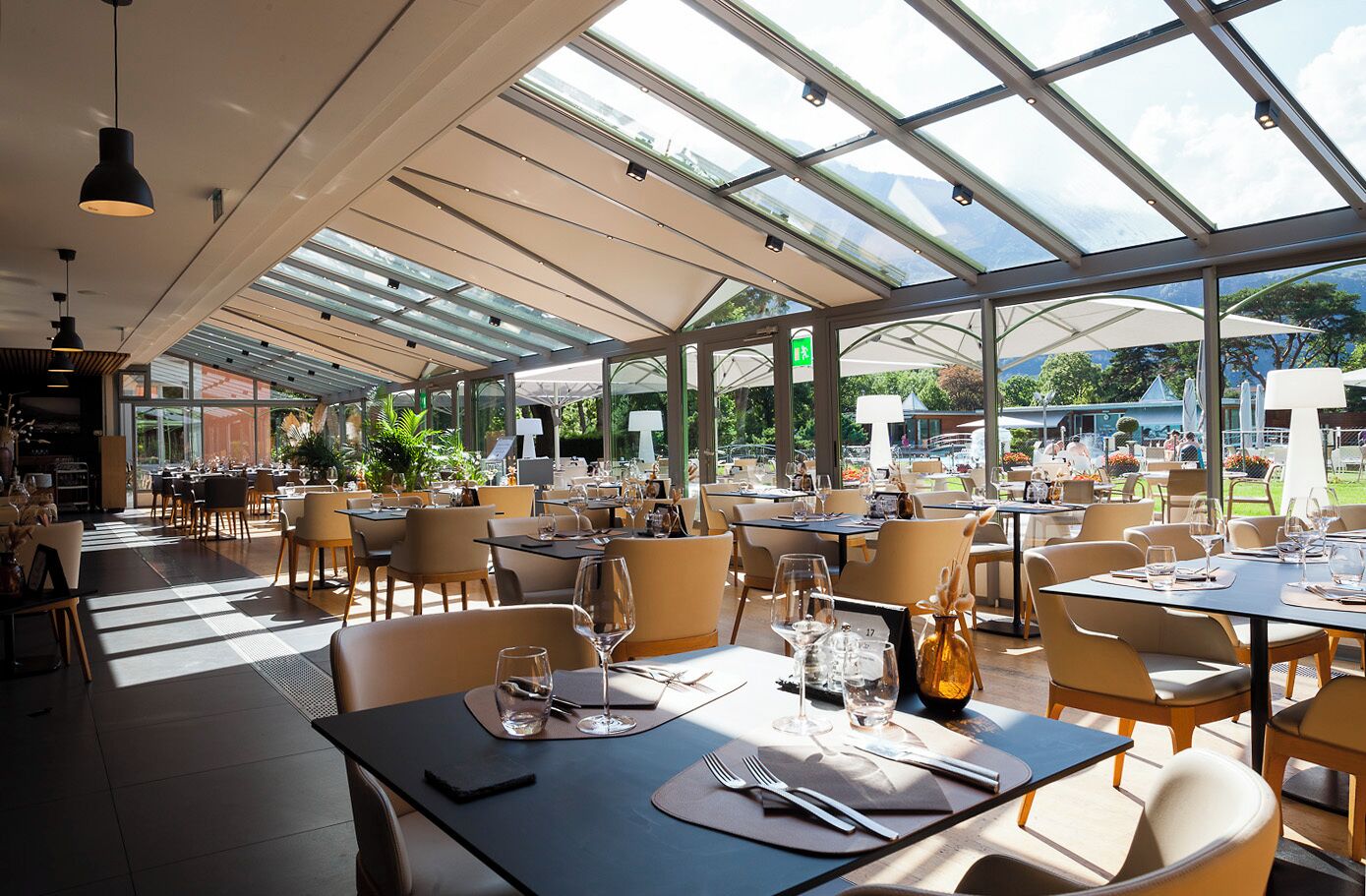 An indoor dining area with tables, chairs, and a glass ceiling allowing natural light.