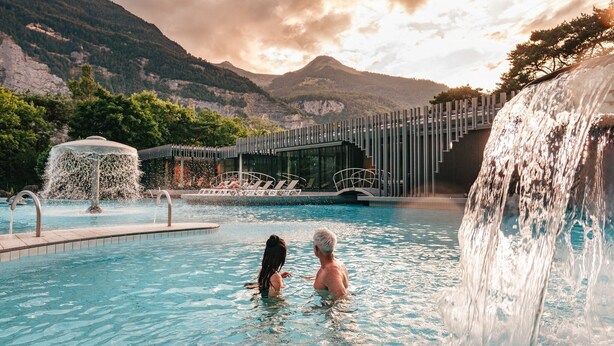 A pool with a waterfall feature, a covered seating area, and a mountain backdrop.