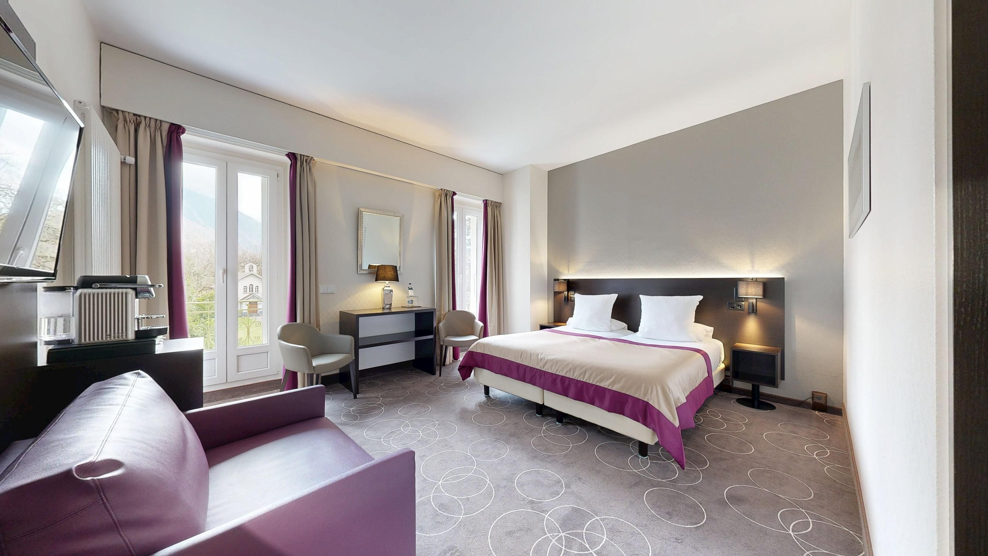 Ein Hotelzimmer mit einem Bett, einem Schreibtisch, einem Sessel, einer Couch und einem großen Fenster.