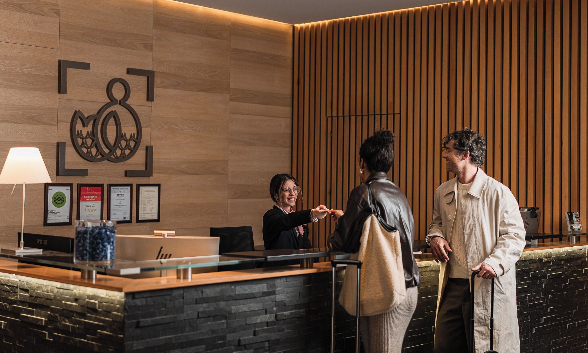 Un mostrador de recepción con pared de paneles de madera, premios enmarcados y una lámpara moderna.