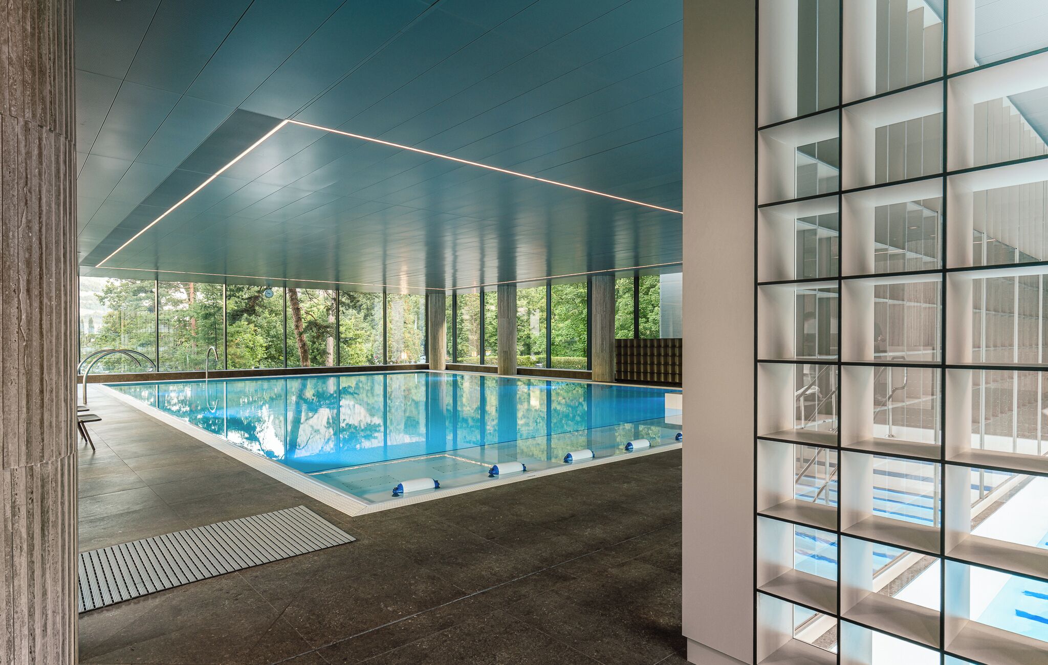 Une piscine intérieure avec de grandes fenêtres donnant sur la forêt.