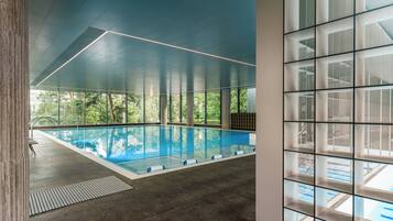 Une piscine intérieure avec de grandes fenêtres donnant sur la forêt.