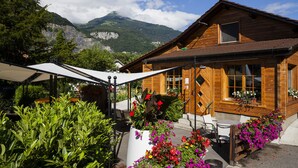 A wooden chalet with a patio area, outdoor seating, and a mountain view.