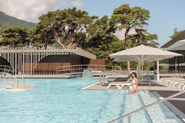 A swimming pool with a waterfall feature, surrounded by trees and lounge chairs.