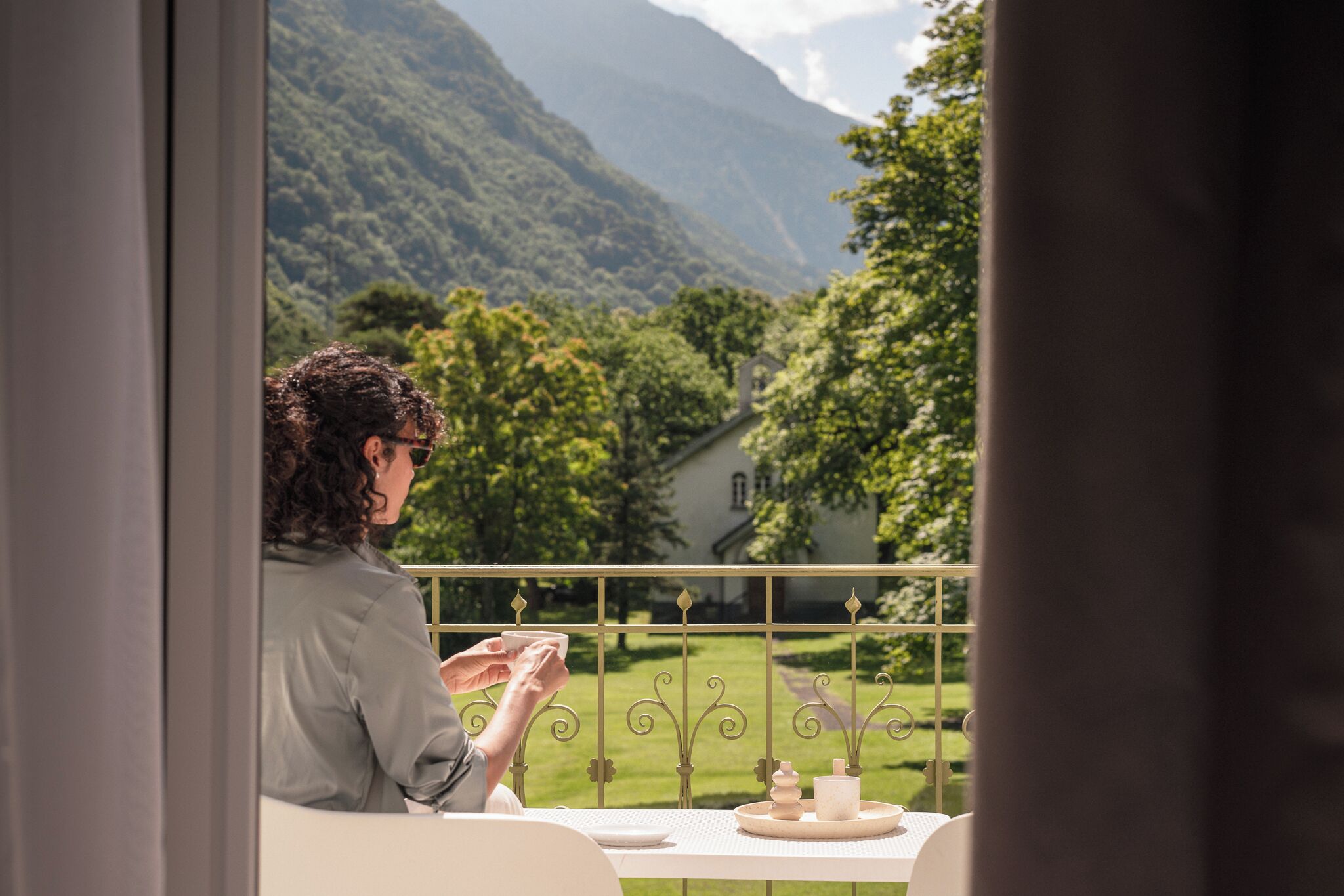 Una persona sentada a una mesa con vistas a un paisaje verde exuberante y montañas al fondo.