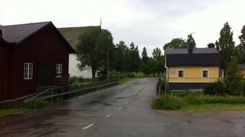 Une route de campagne, avec un bâtiment rouge sur la gauche et un bâtiment jaune sur la droite.