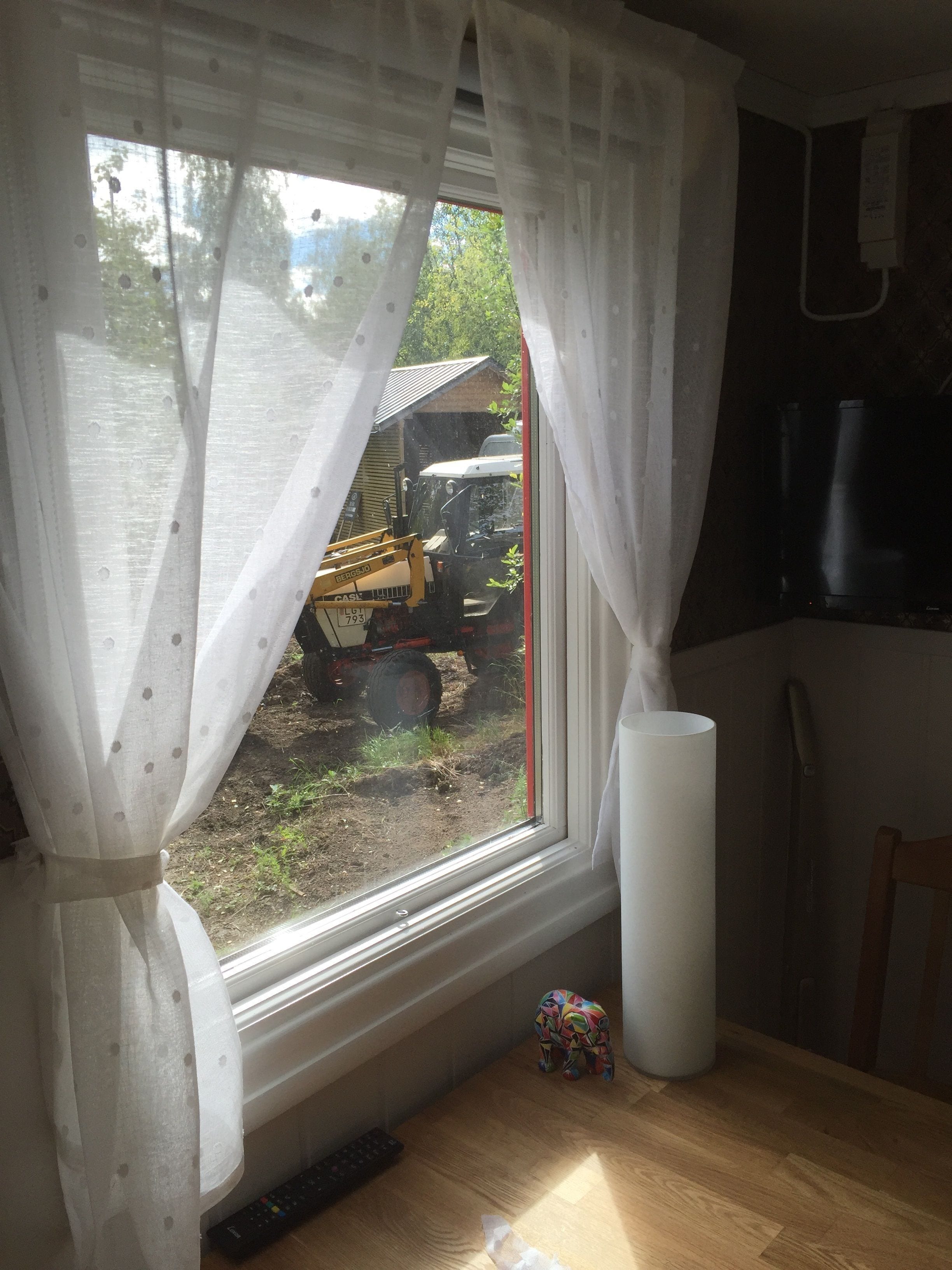 Una ventana con cortinas blancas, un control remoto y un juguete colorido en el alféizar.