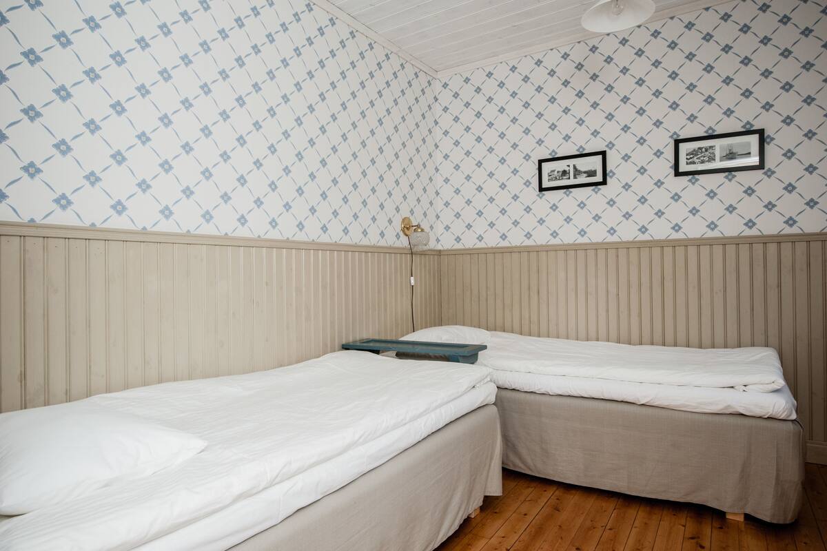 Una habitación con dos camas individuales, piso de madera y papel tapiz estampado.