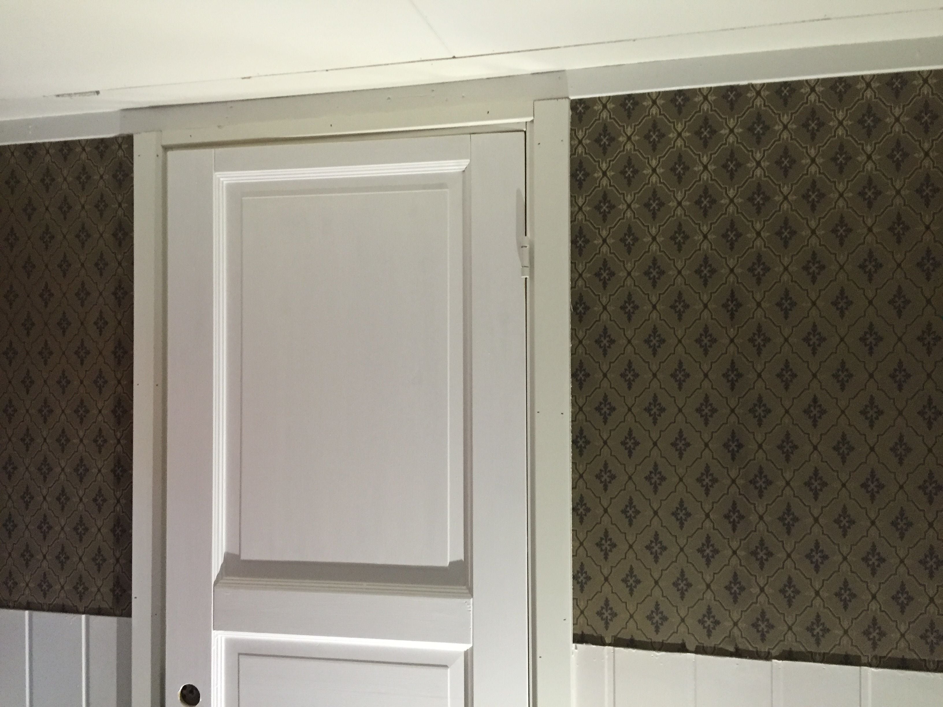 A white door with a panelled design, flanked by wallpapered walls with a diamond pattern.
