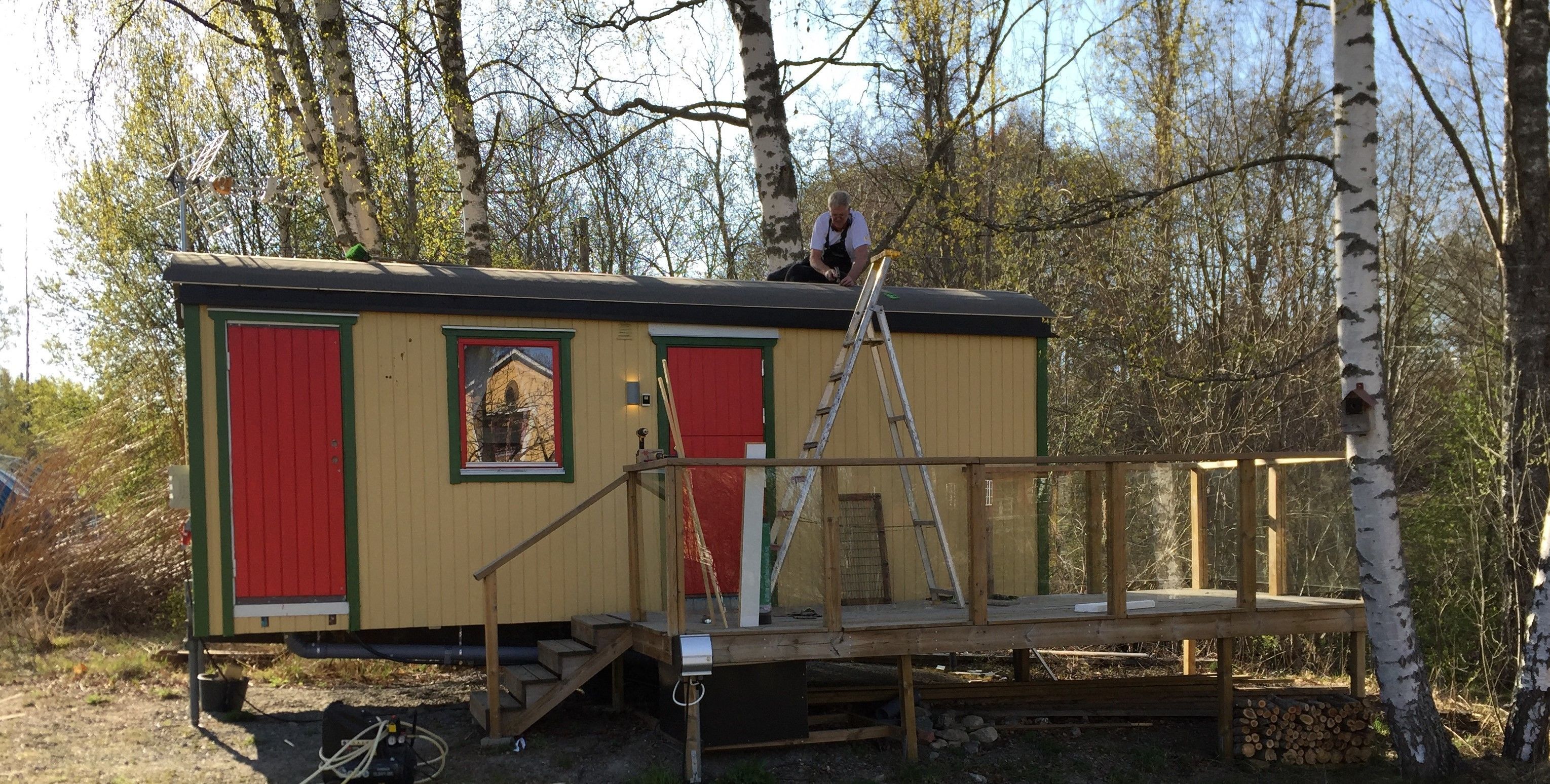 A small, single-story cabin with a red door and windows, a wooden deck, and a ladder.