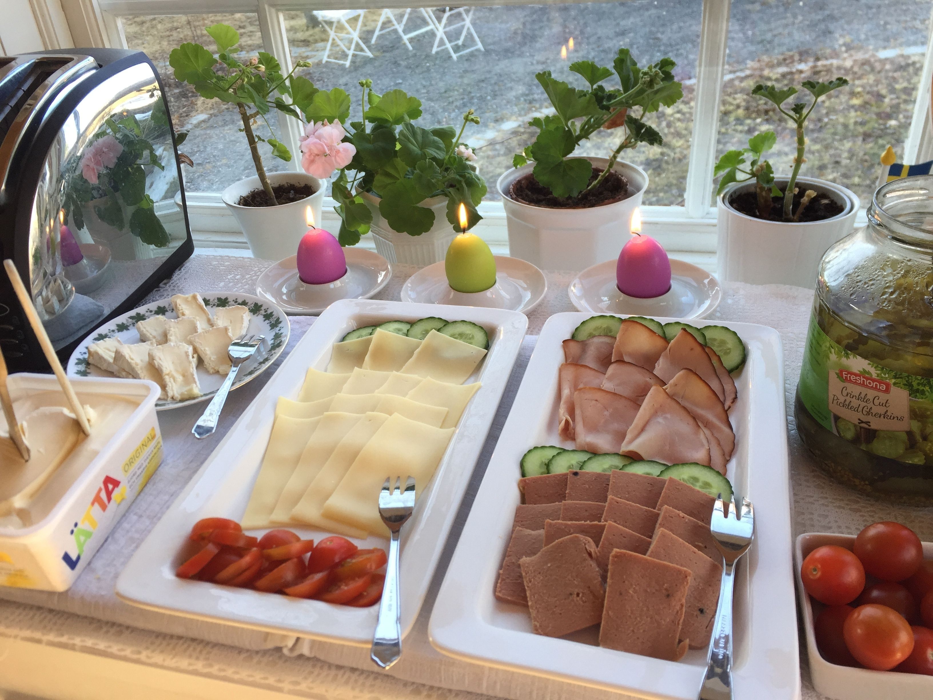A breakfast buffet with various food items and potted plants on a table by a window.