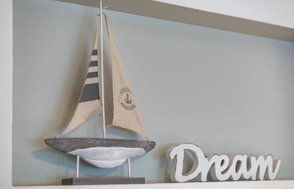 A sailboat model with a tag hanging from it, placed on a shelf next to a word 'Dream'.