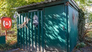 Un cobertizo utilitario verde con puerta y cerradura de metal, y un ventanal pequeño.