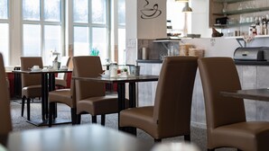 Un interior de restaurante moderno con mesas altas, sillas, ventanas amplias y una cocina a la vista.