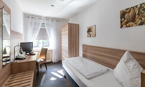A hotel room with a bed, a desk with a computer, a chair, a radiator, and a window with sheer curtains. - Stadt-gut-Hotel Großer Kurfürst (Emden)