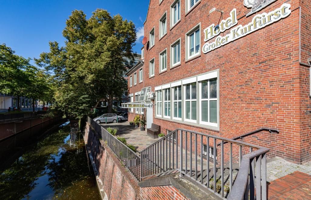 Un hotel con fachada de ladrillo rojo, un letrero que dice 'Hotel Großer Kurfürst' y un canal al frente.