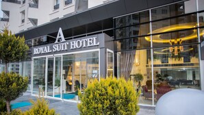 Exterior do Hotel Royal Suit com fachada de vidro moderna, área externa bem cuidada com plantas em vasos e vista clara do interior através do vidro.