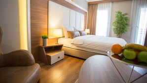 Quarto de hotel moderno com uma cama grande, mesas de cabeceira, uma pequena planta e uma cesta de frutas no criado-mudo.