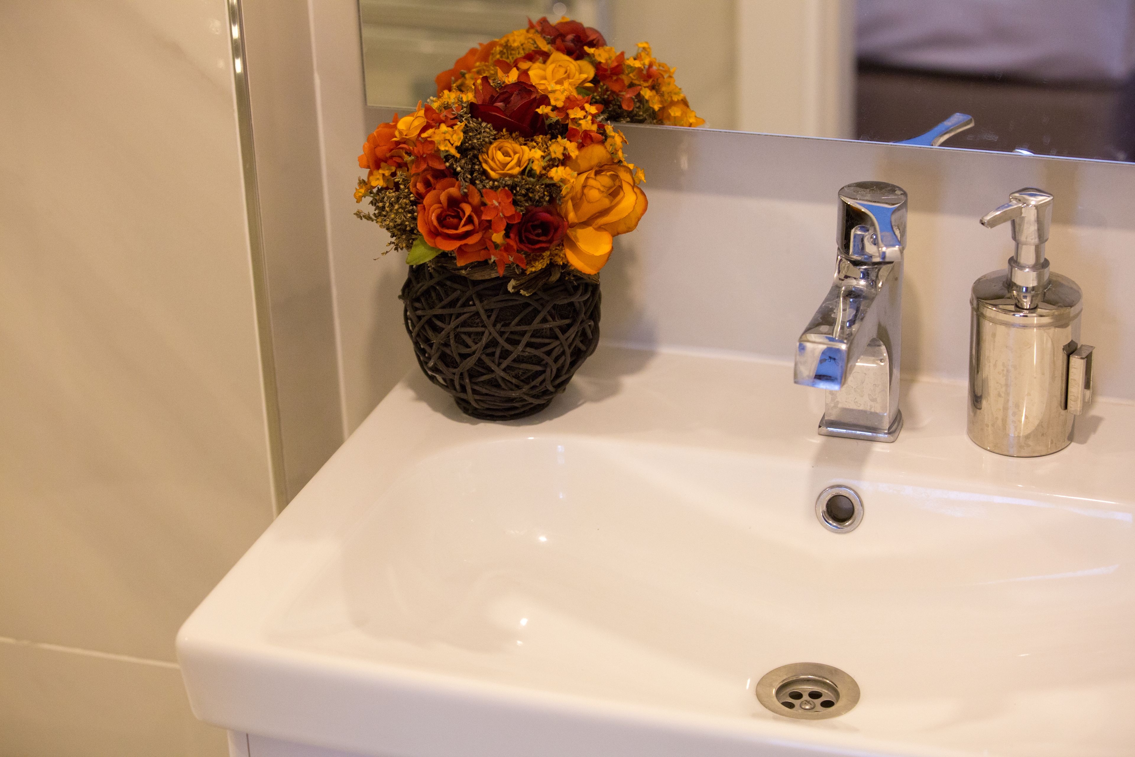A bathroom sink with a mirror, a vase of flowers, and a soap dispenser.