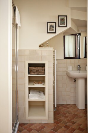 A bathroom with a shower, a sink, and a shelf with baskets and towels. - Locanda San Bernardo (Vigevano)