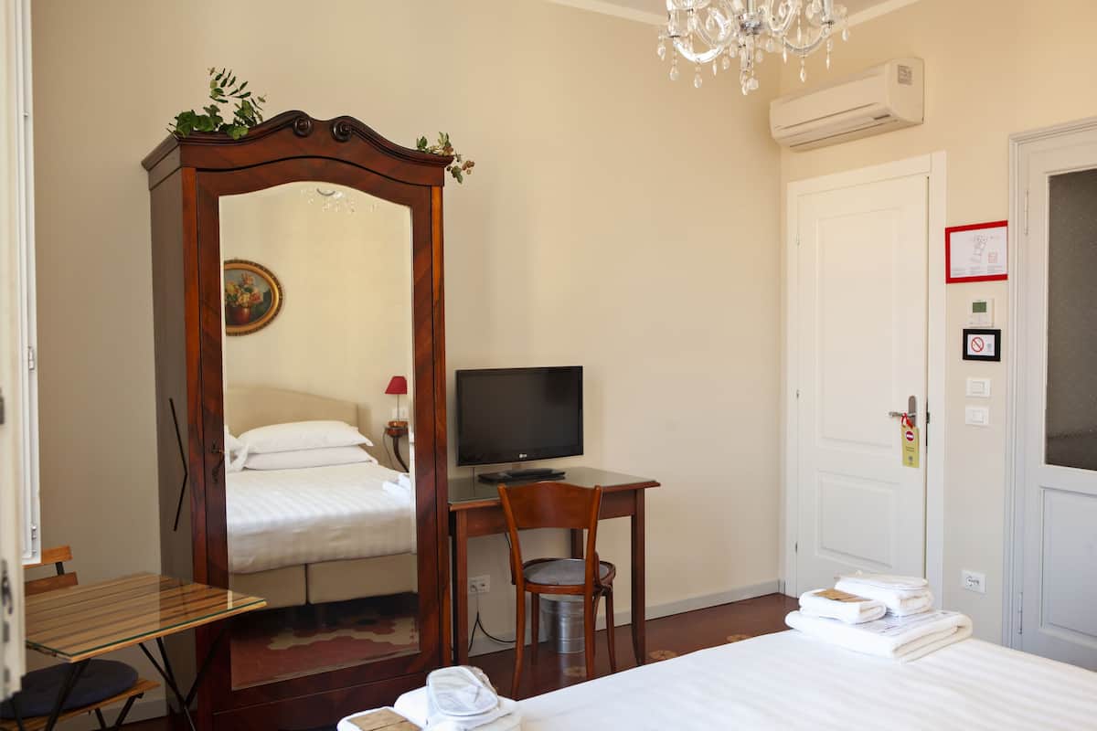 A hotel room with a bed, a desk with a computer, a chair, a mirror, and a chandelier.