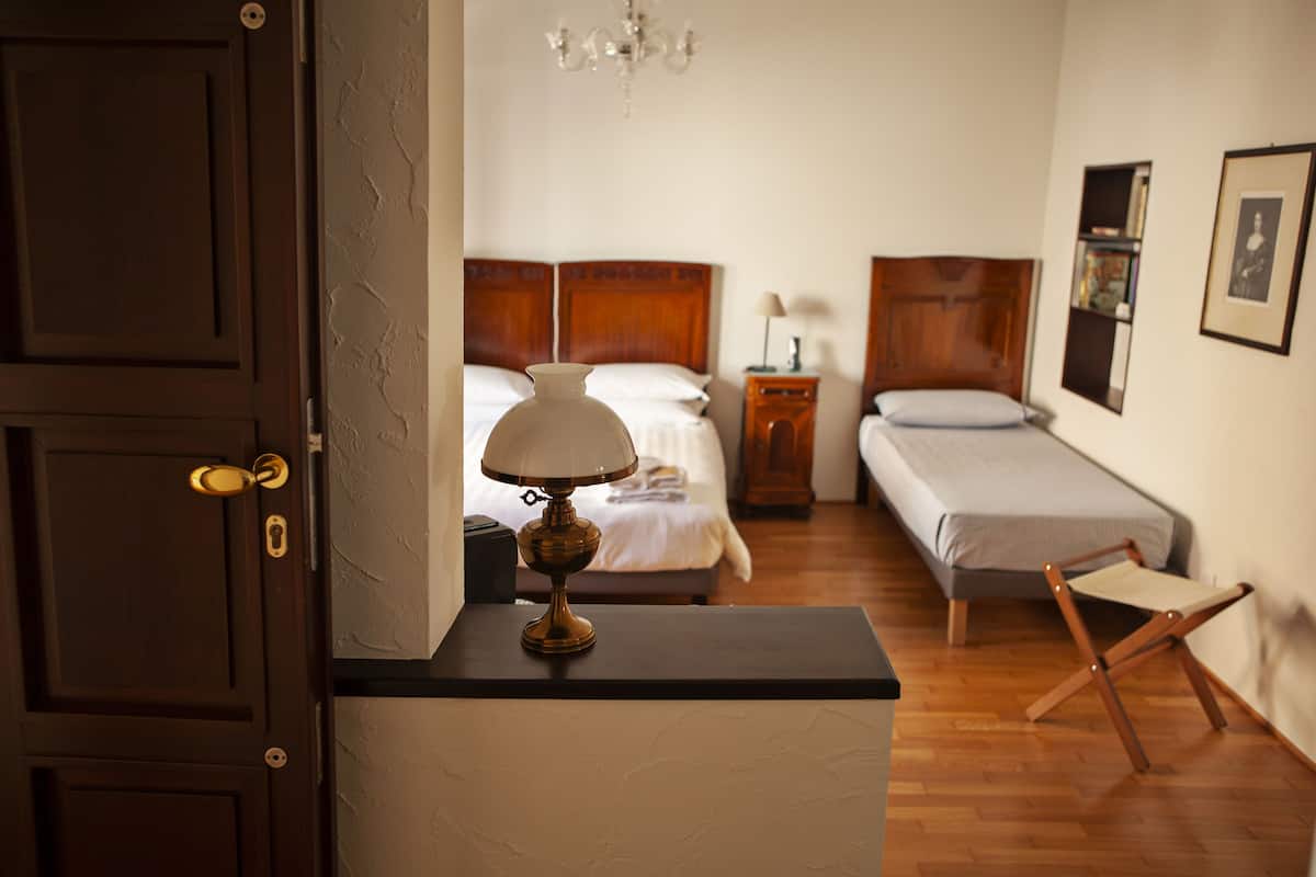 A hotel room with two beds, a bedside table with a lamp, a wooden chair, and a door.