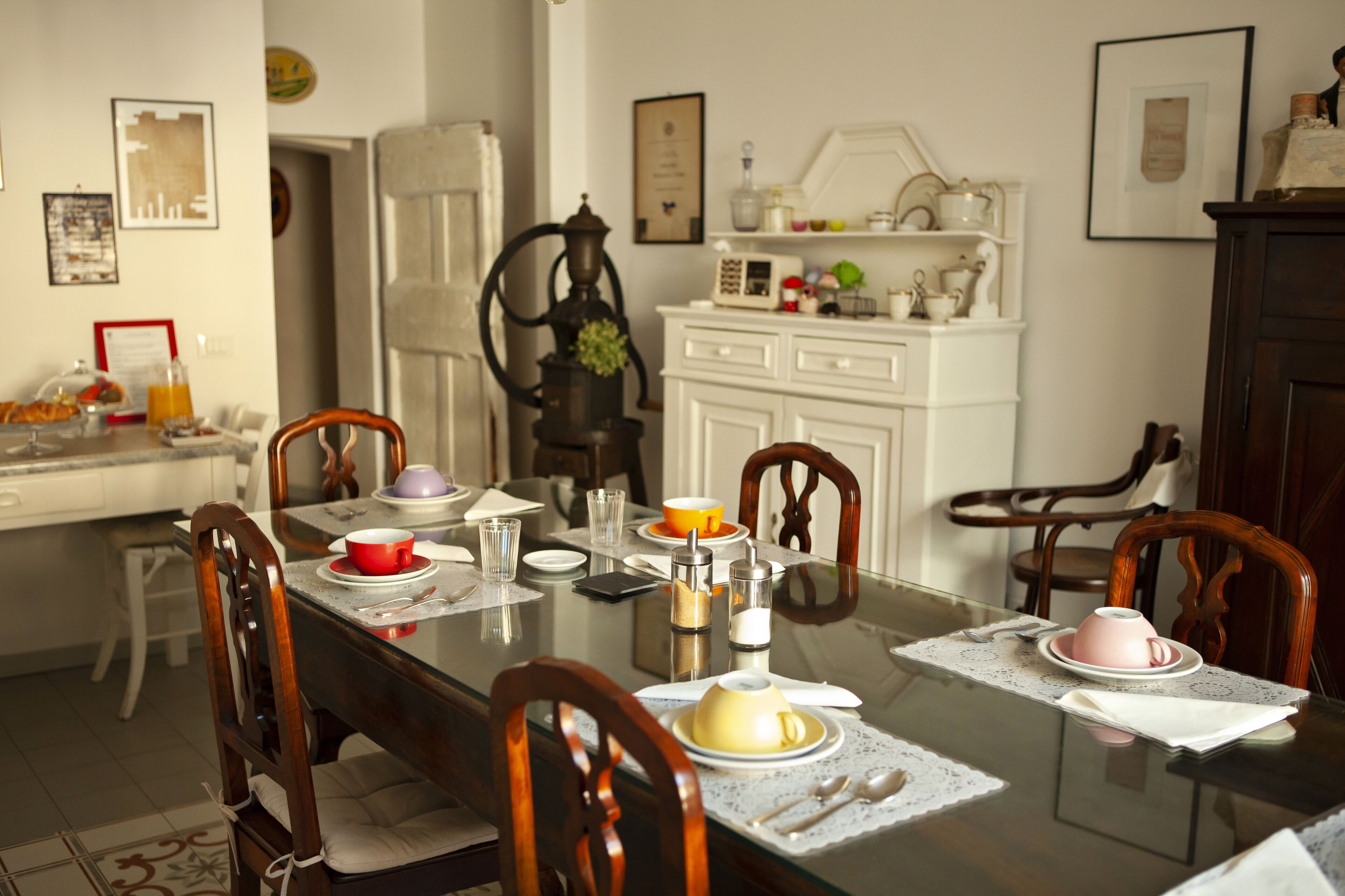 A dining table set with plates, cups, and cutlery, surrounded by wooden chairs.