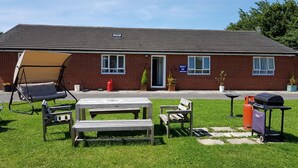 A brick building with a flat roof, a swing chair, a picnic table, a bench, and a barbecue grill in the yard. - Chelford Guesthouse (Knutsford)